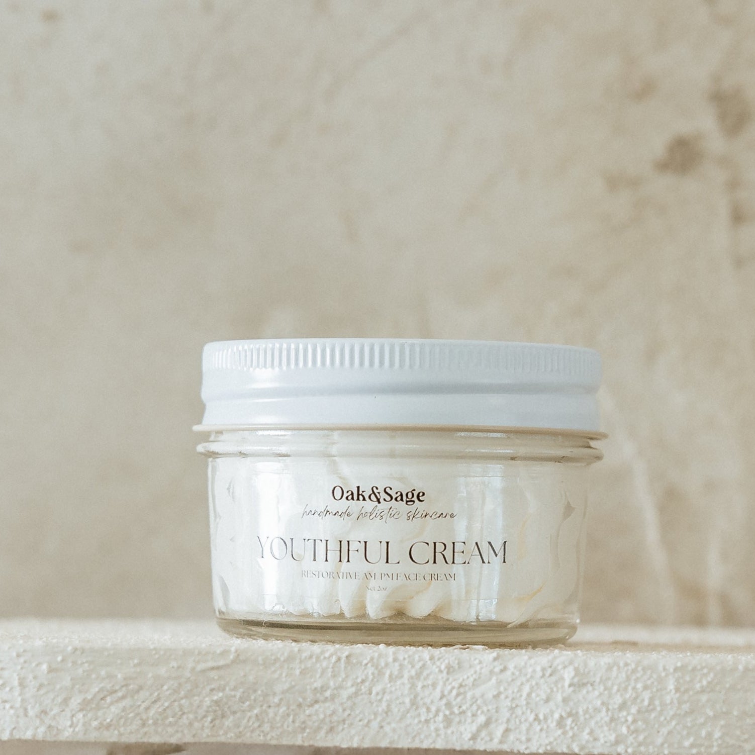 Oak & Sage Youthful Cream in a glass jar with white lid, displayed on a natural stone surface—restorative anti-aging face cream with a whipped, buttery texture.