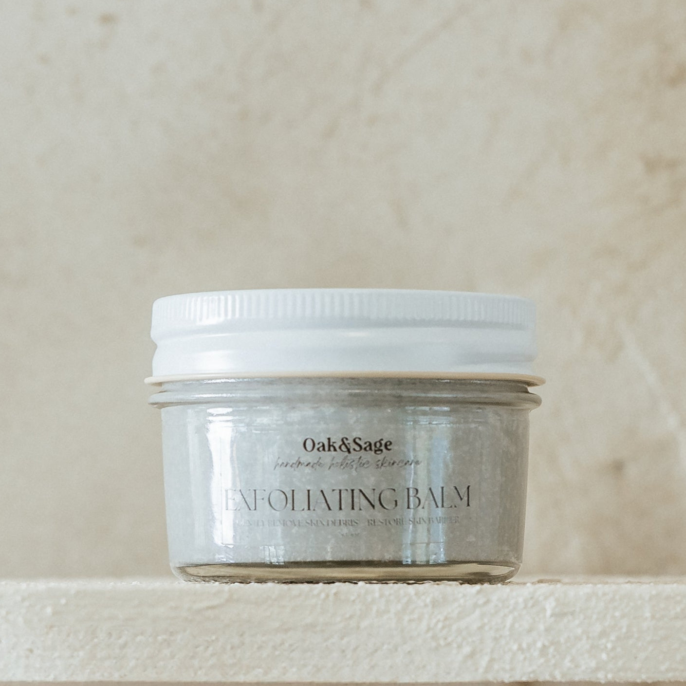 Oak & Sage Exfoliating Balm in glass jar, formulated with fine pumice, tallow, and calendula to gently remove dead skin and support skin barrier health.