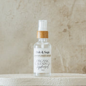 Oak & Sage Calendula Hydrosol in glass spray bottle with bamboo top, displayed on white pedestal against marbled stone background.