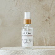 Oak & Sage Organic Calendula Hydrosol in glass spray bottle with bamboo top, displayed on white textured pedestal against warm marbled background.