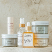 Oak & Sage Ultimate Skincare Set displayed on neutral stone backdrop, featuring natural tallow-based products including Radiant Serum, Cleansing Balm, Exfoliating Balm, Youthful Cream, Organic Rose Hydrosol, and Vanilla Lip Balm.