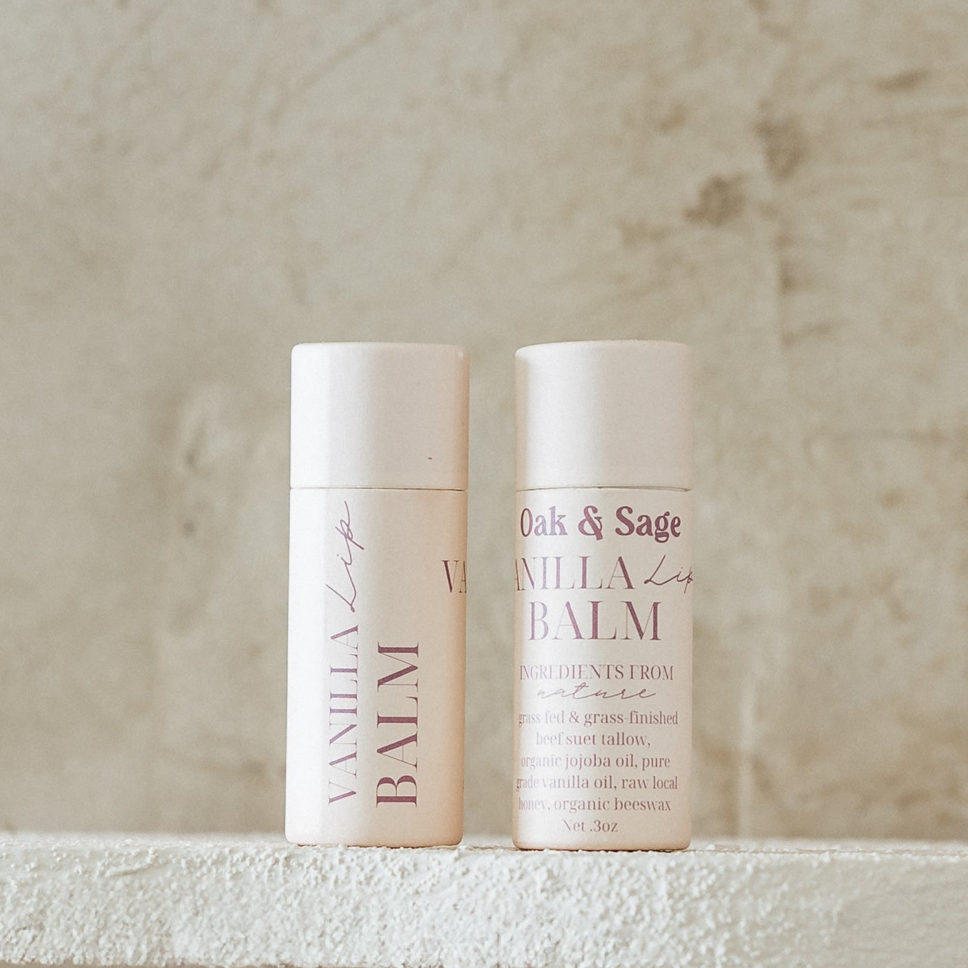 Oak & Sage Vanilla Lip Balm duo with eco-friendly paper tubes, featuring clean, natural ingredients like tallow, jojoba oil, vanilla, honey, and beeswax, styled against a neutral stone background.