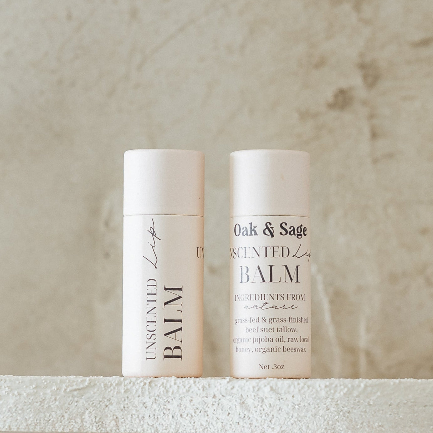 Oak & Sage Unscented Lip Balm duo with eco-friendly paper tubes, featuring clean, natural ingredients like tallow, jojoba oil, vanilla, honey, and beeswax, styled against a neutral stone background.