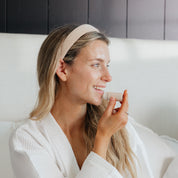 Woman in a white robe applying Oak & Sage Vanilla Lip Balm with a smile, highlighting natural skincare and eco-conscious beauty in a cozy morning routine.