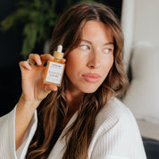 Woman in white robe holding Oak & Sage Radiant Serum, showcasing natural skincare glow and radiant complexion benefits.