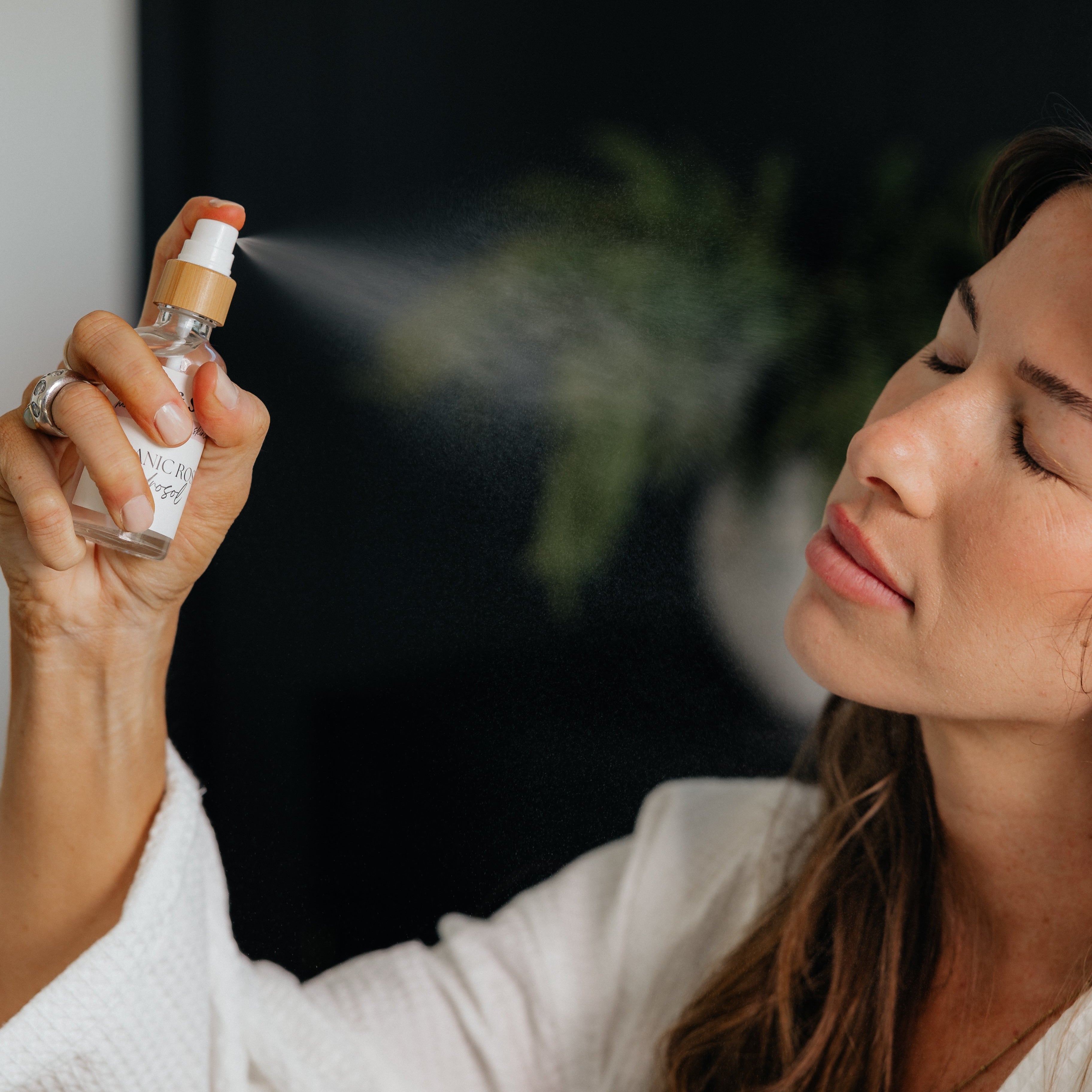 Woman misting face with non-toxic Oak & Sage Rose Hydrosol, demonstrating gentle application of natural facial toner in skincare routine.