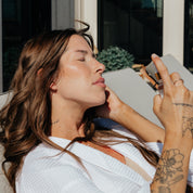 Woman misting face with Oak & Sage organic hydrosol toner while lounging outdoors, showcasing natural skincare routine and sun-safe hydration.