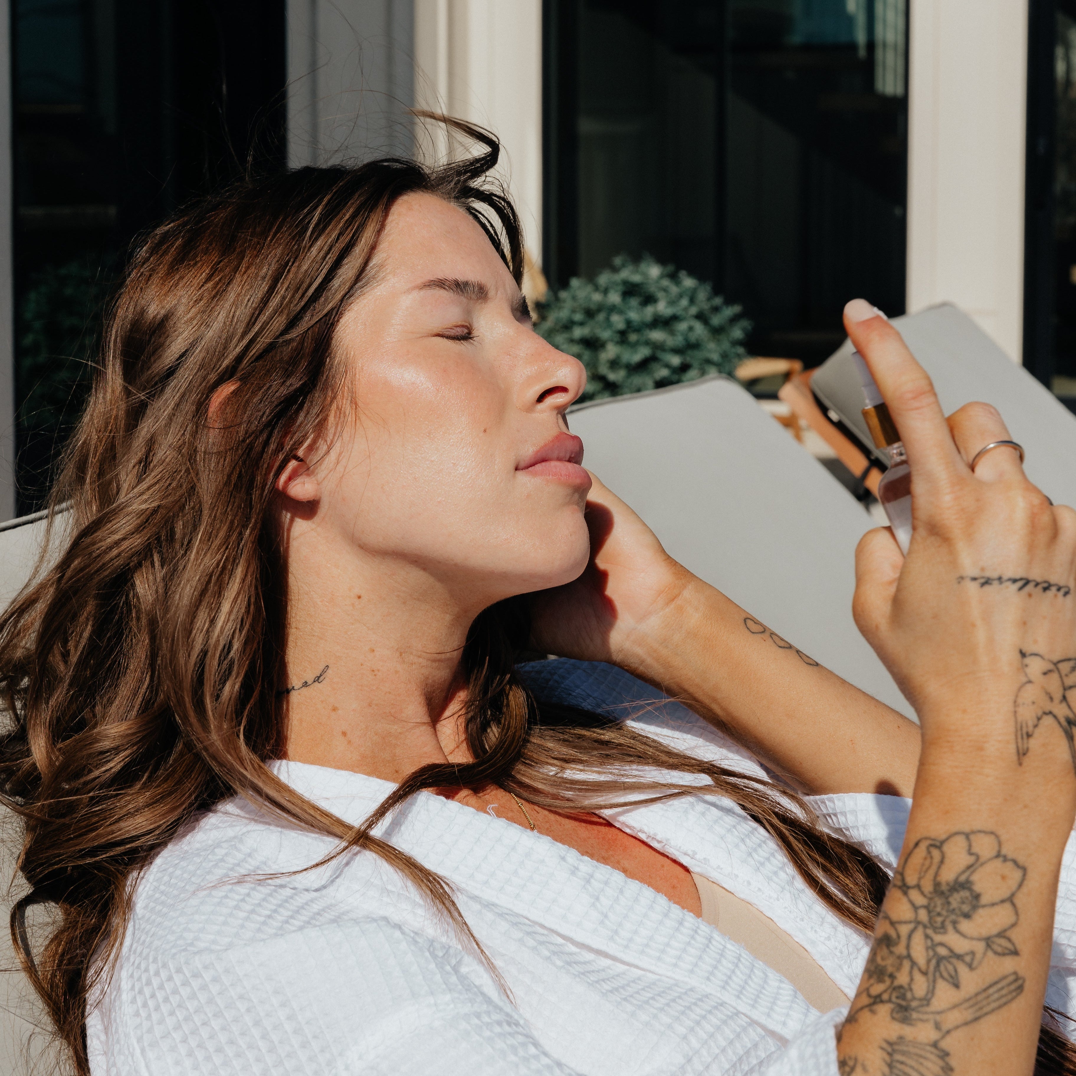 Woman misting face with Oak & Sage organic hydrosol toner while lounging outdoors, showcasing natural skincare routine and sun-safe hydration.