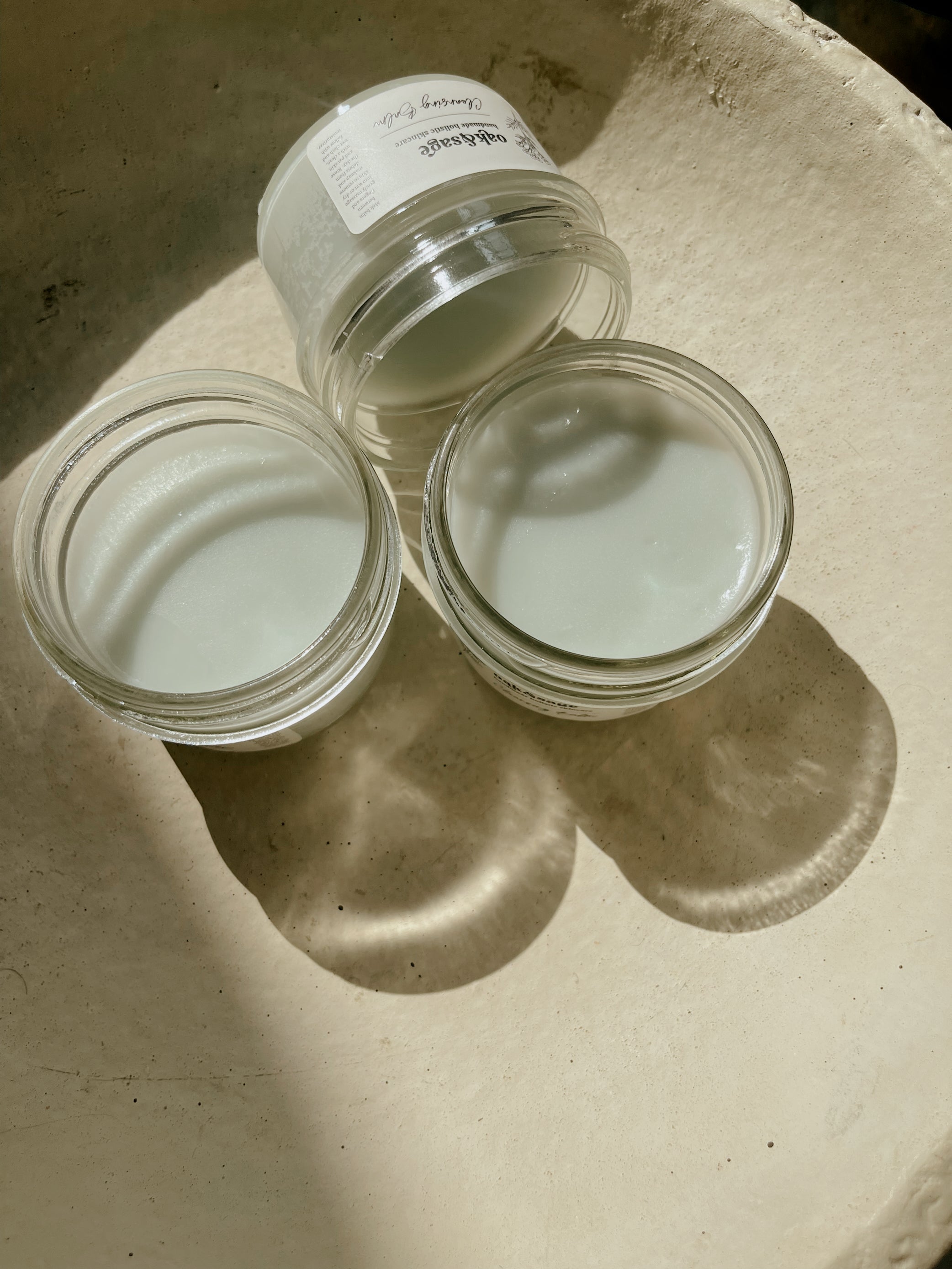Three jars of Oak & Sage Cleansing Balm open to reveal creamy, tallow-based formula – natural face cleanser in sunlight on neutral background.