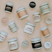 Top view of Oak & Sage Everywhere Cream jars and travel tins in multiple natural scents like Backwoods, Warm Vanilla, Unscented, and Eucalyptus Lavender—nourishing tallow-based body butter displayed on neutral stone background