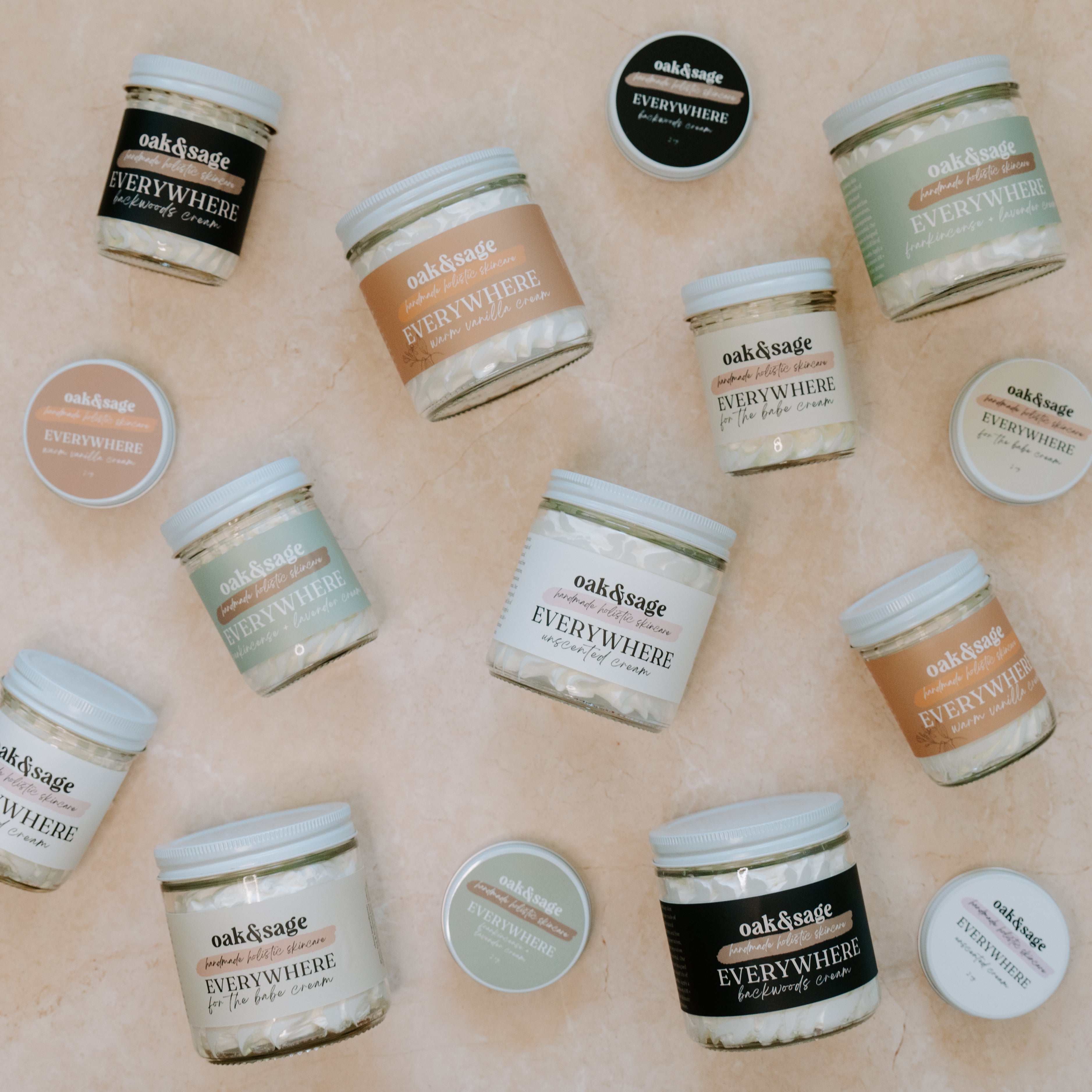 Top view of Oak & Sage Everywhere Cream jars and travel tins in multiple natural scents like Backwoods, Warm Vanilla, Unscented, and Eucalyptus Lavender—nourishing tallow-based body butter displayed on neutral stone background