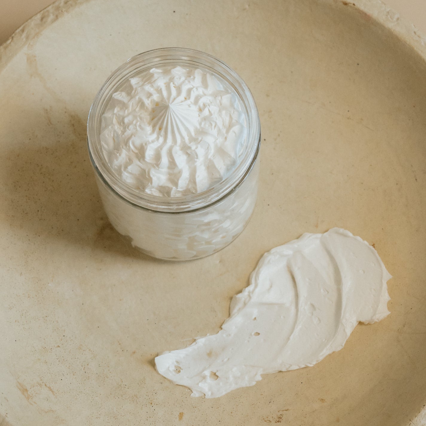 Open jar of Oak & Sage Everywhere Cream showing whipped, airy texture with a smooth swipe of nourishing tallow body butter on a neutral ceramic plate.