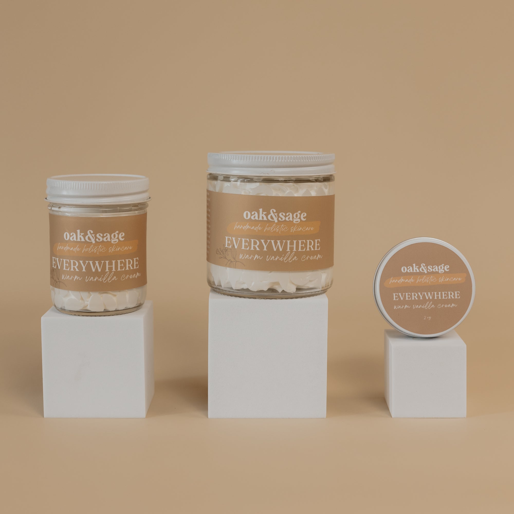 Oak & Sage Everywhere Cream in Warm Vanilla scent displayed in three sizes—large jar, medium jar, and travel tin—on minimalist white pedestals against a warm beige background