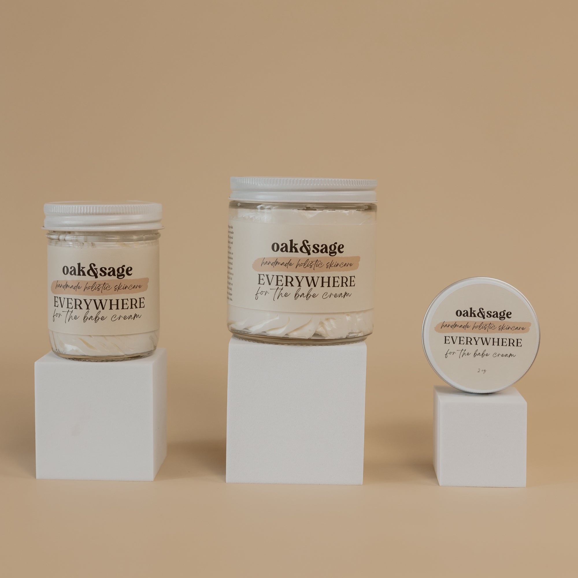 Oak & Sage Everywhere Cream in For The Babe scent displayed in three sizes—large jar, medium jar, and travel tin—on minimalist white pedestals against a warm beige background