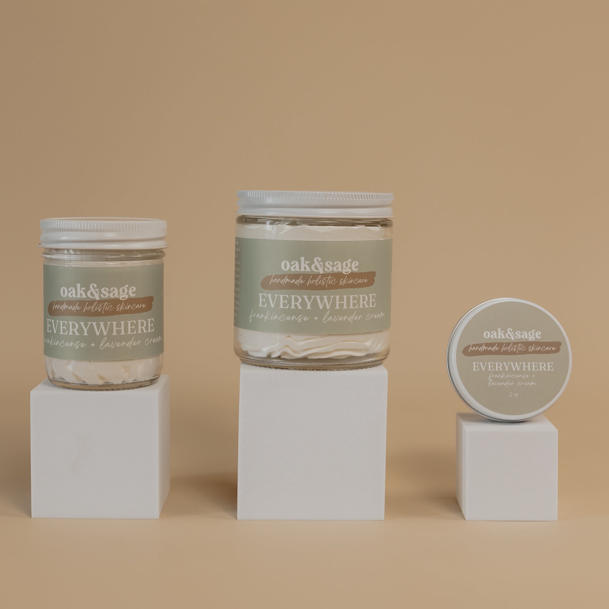 Oak & Sage Everywhere Cream in Frankincense & Lavender  scent displayed in three sizes—large jar, medium jar, and travel tin—on minimalist white pedestals against a warm beige background