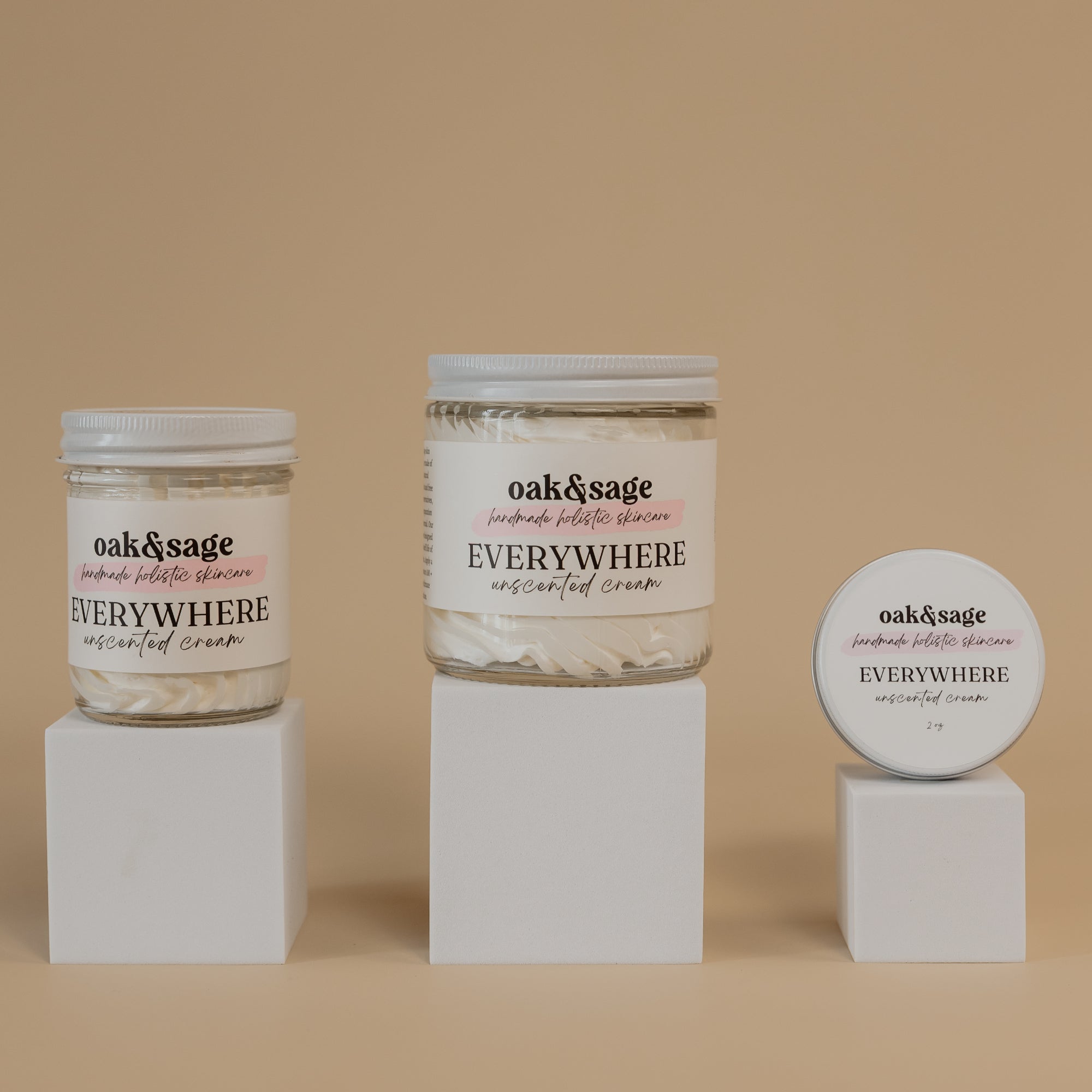 Oak & Sage Everywhere Cream in Unscented scent displayed in three sizes—large jar, medium jar, and travel tin—on minimalist white pedestals against a warm beige background