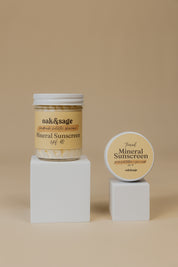 Oak & Sage Mineral Sunscreen SPF 40 in 8 oz glass jar and 2 oz travel tin, displayed on white pedestals against neutral beige background.