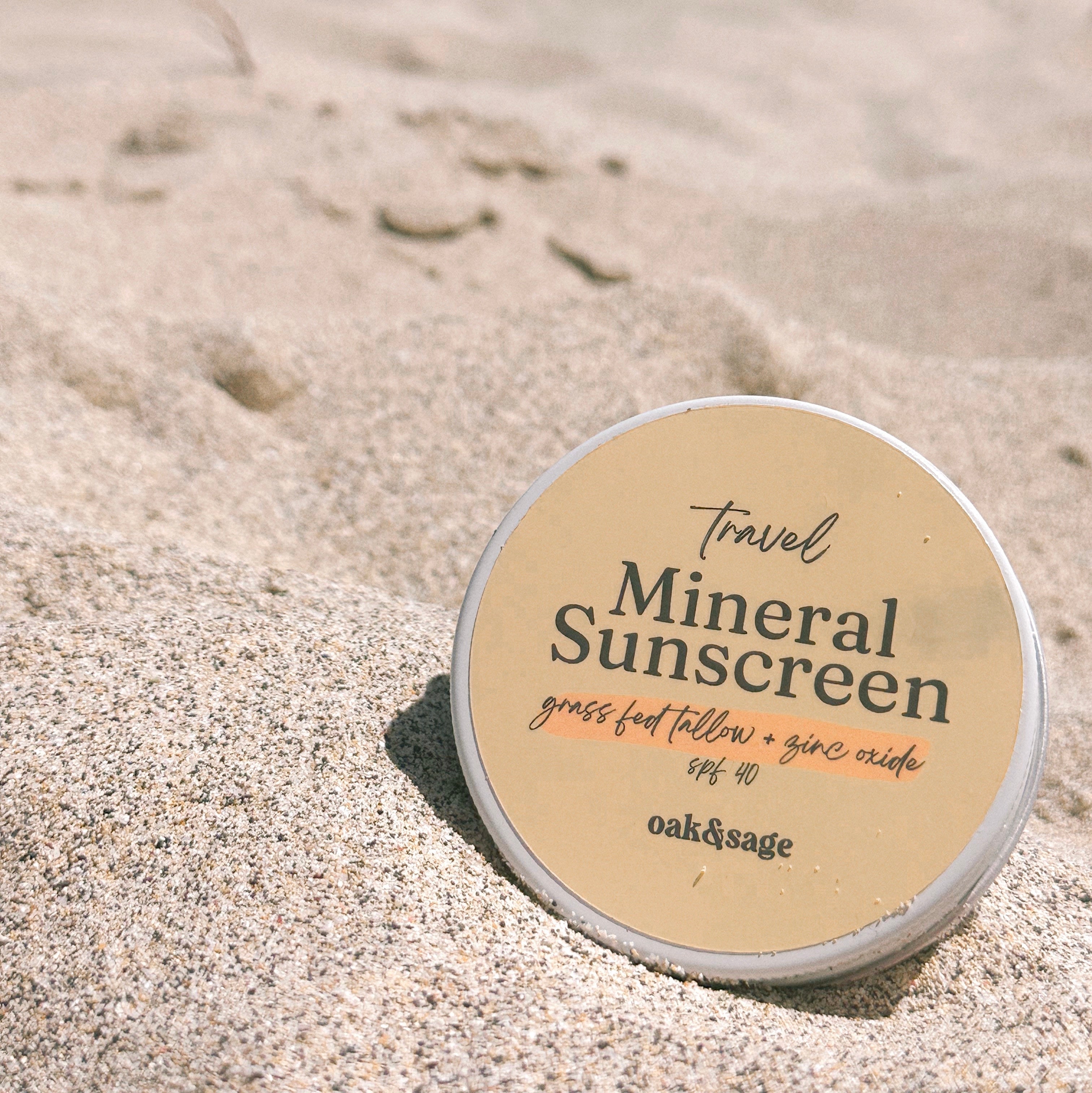 Oak & Sage Travel Mineral Sunscreen SPF 40 tin with grass-fed tallow and zinc oxide, photographed on sandy beach for natural sun protection lifestyle.