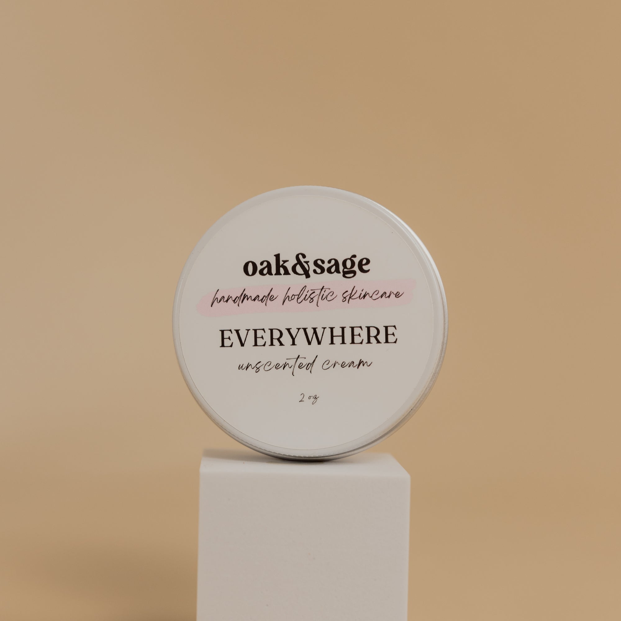 Oak & Sage Unscented Everywhere Cream in a 2 oz travel-size tin, displayed on a modern white pedestal against a neutral beige background