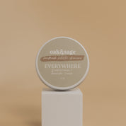 Oak & Sage Frankincense & Lavender  Everywhere Cream in a 2 oz travel-size tin, displayed on a modern white pedestal against a neutral beige background