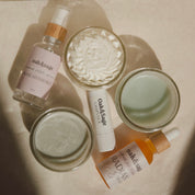 Flat lay of Oak & Sage Ultimate Skincare Set including Radiant Serum, Rose Hydrosol, Youthful Cream, Cleansing Balm, Exfoliating Balm, and natural tallow-based lip balm on neutral background.