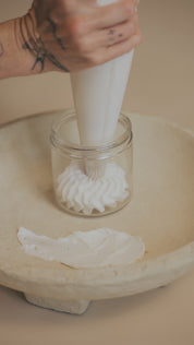 Artisan hand-piping Oak & Sage Everywhere Cream into a clear glass jar, showcasing its rich whipped texture and silky tallow body butter consistency